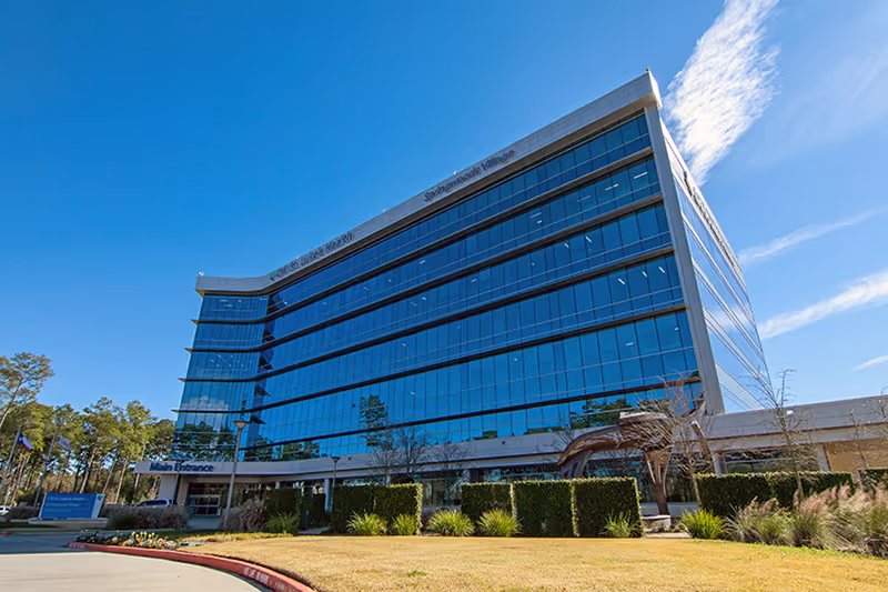 A large glass-front medical clinic building with a curved entrance and landscaped front.