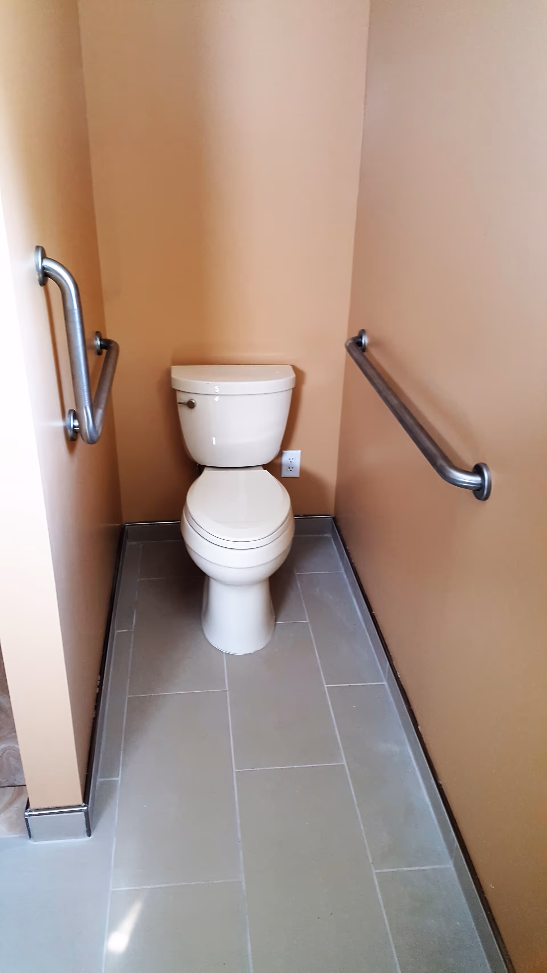 Small accessible bathroom featuring a toilet and sturdy grab bars on both walls.