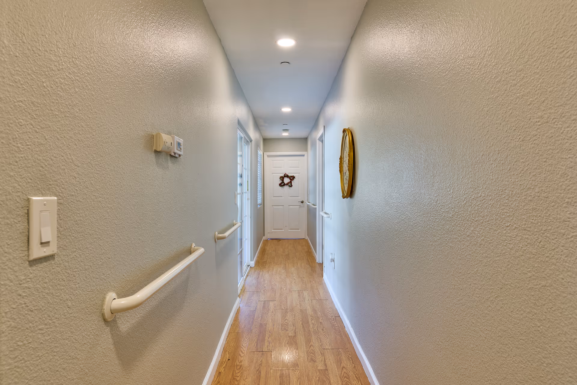 Long hallway with light blue walls, wood floor, and wall-mounted handrails.