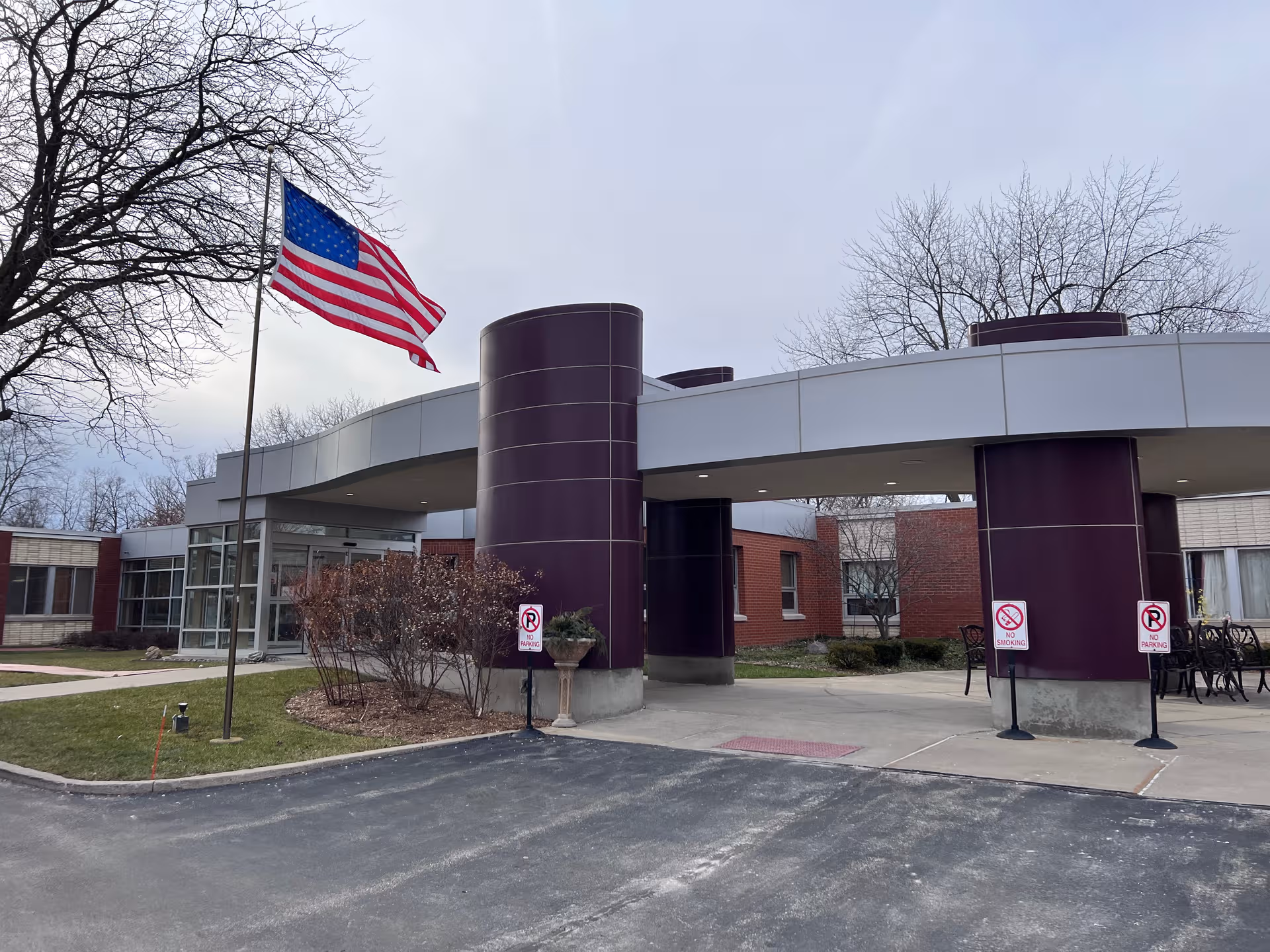 Front view of a senior care facility with a curved canopy, purple pillars, and American flag.