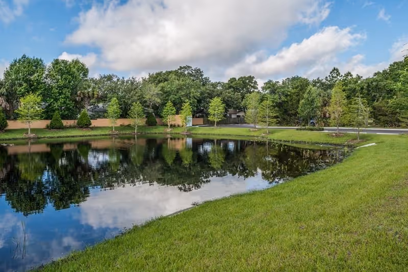 Distant Seasons Largo facility across a serene pond, bordered by trees and green grass.