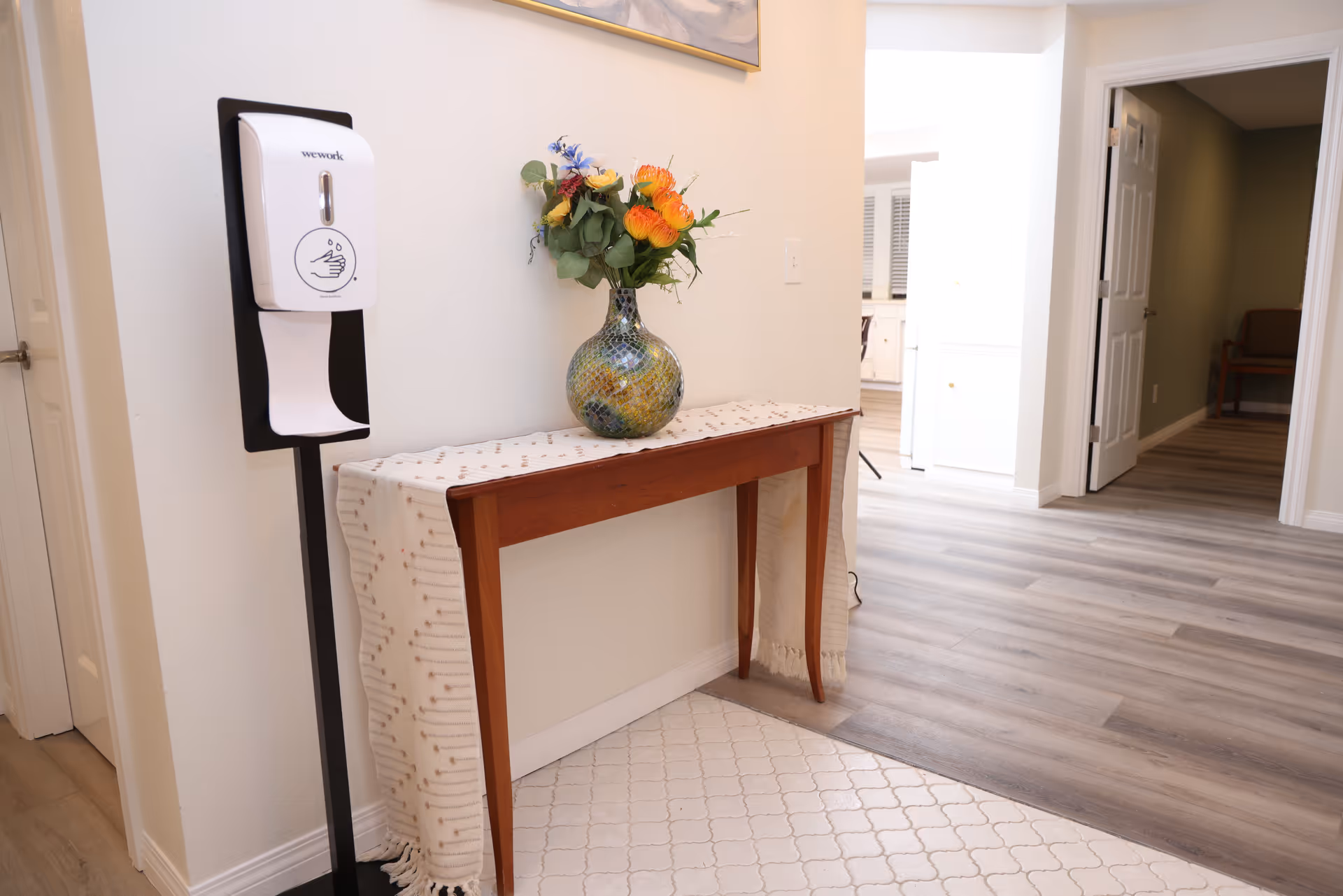 Hallway interior with console table, floral vase, and wall-mounted sanitizer.