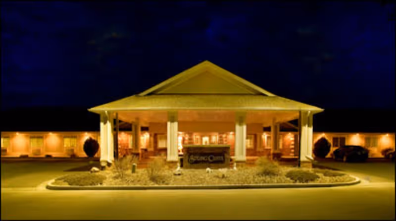 Front entrance of a senior living facility at night with a lit porte-cochère and landscaped driveway.