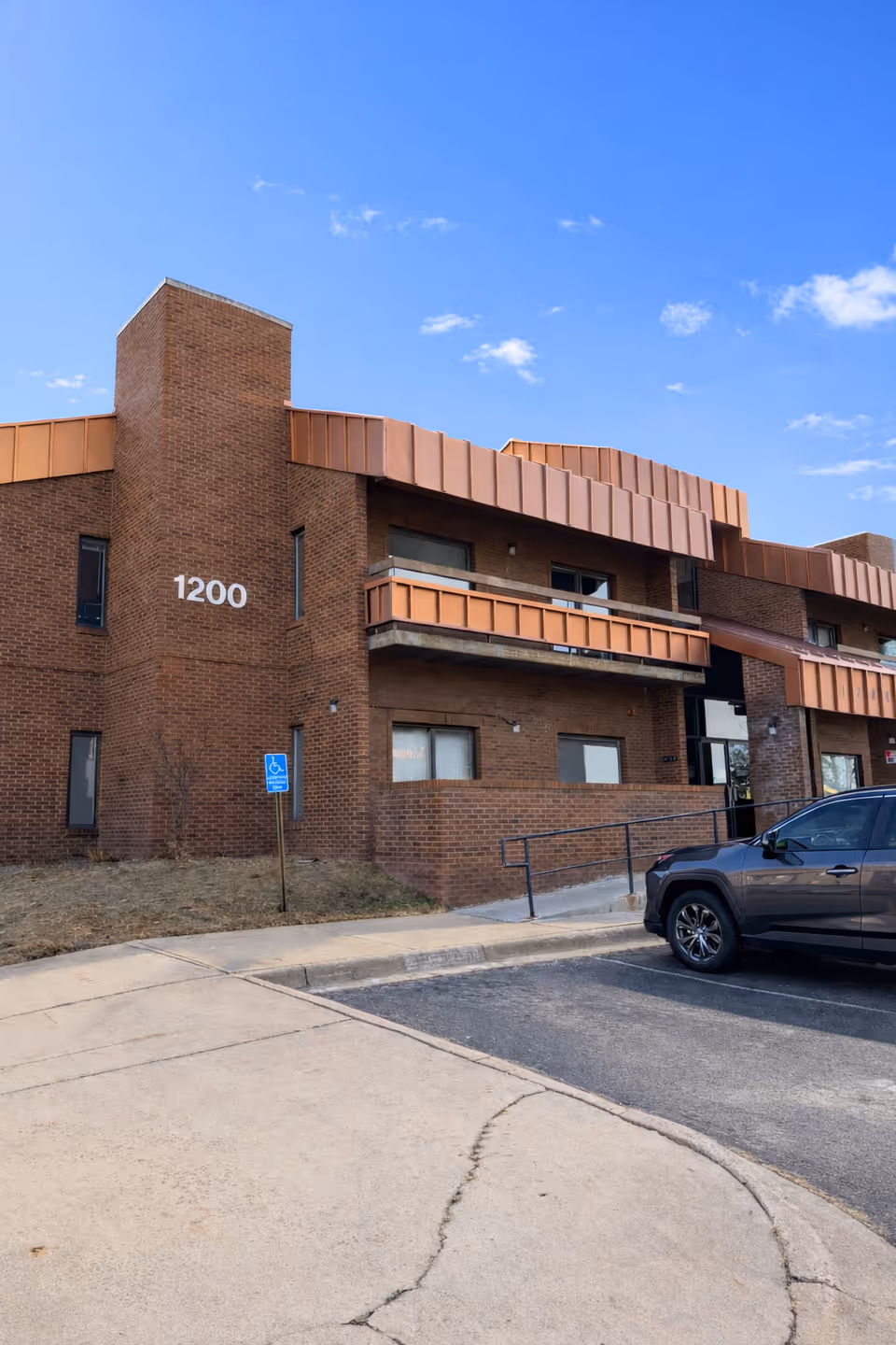Brick senior living facility with number 1200, parking, and clear blue sky.