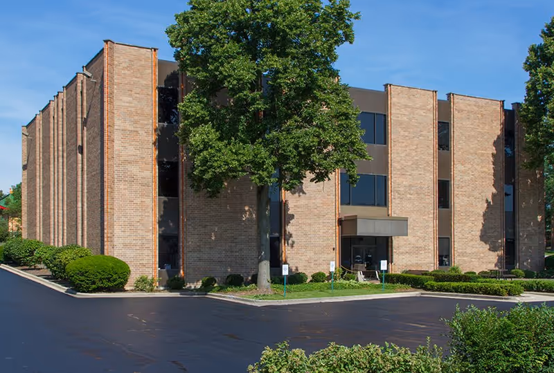 Exterior view of a brick senior living facility with trees and parking.