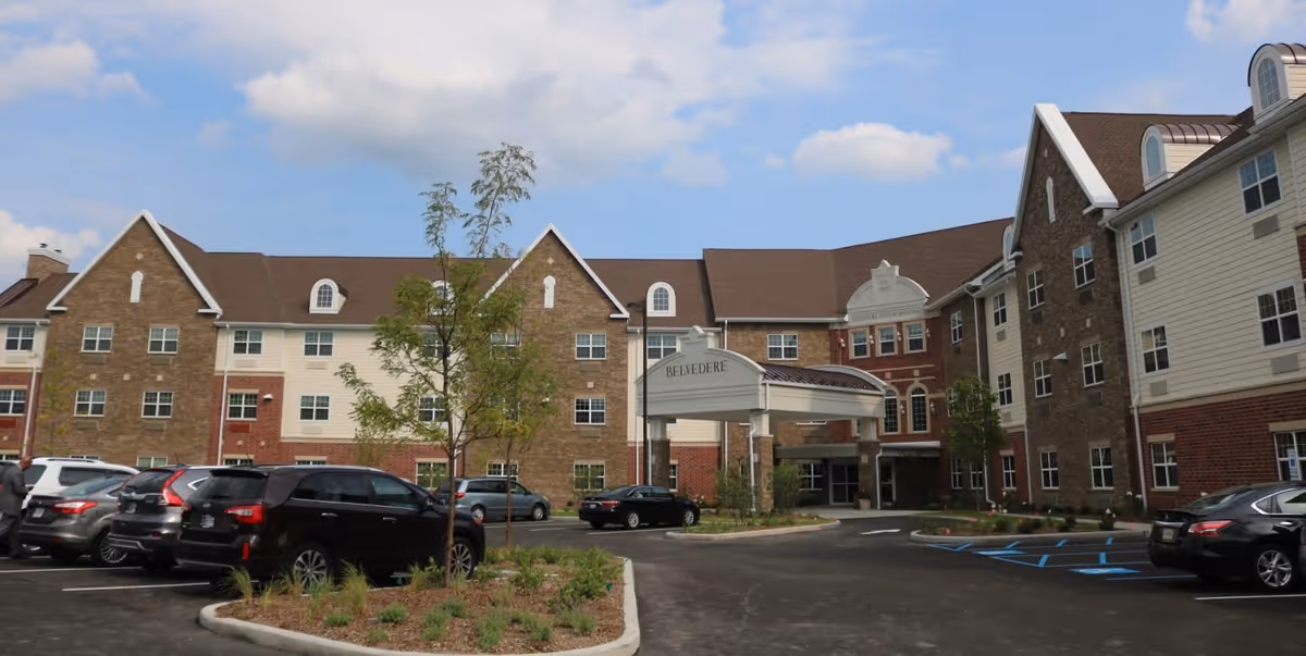 Exterior front entrance of the Belvedere Senior Housing building with a porte-cochère and parked cars in the driveway.