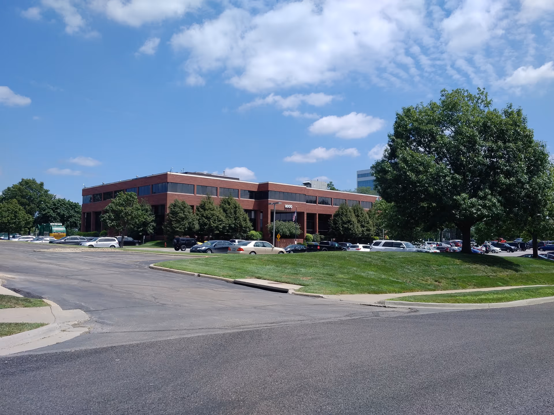 Brick nursing facility with parking lot, trees, and blue sky.