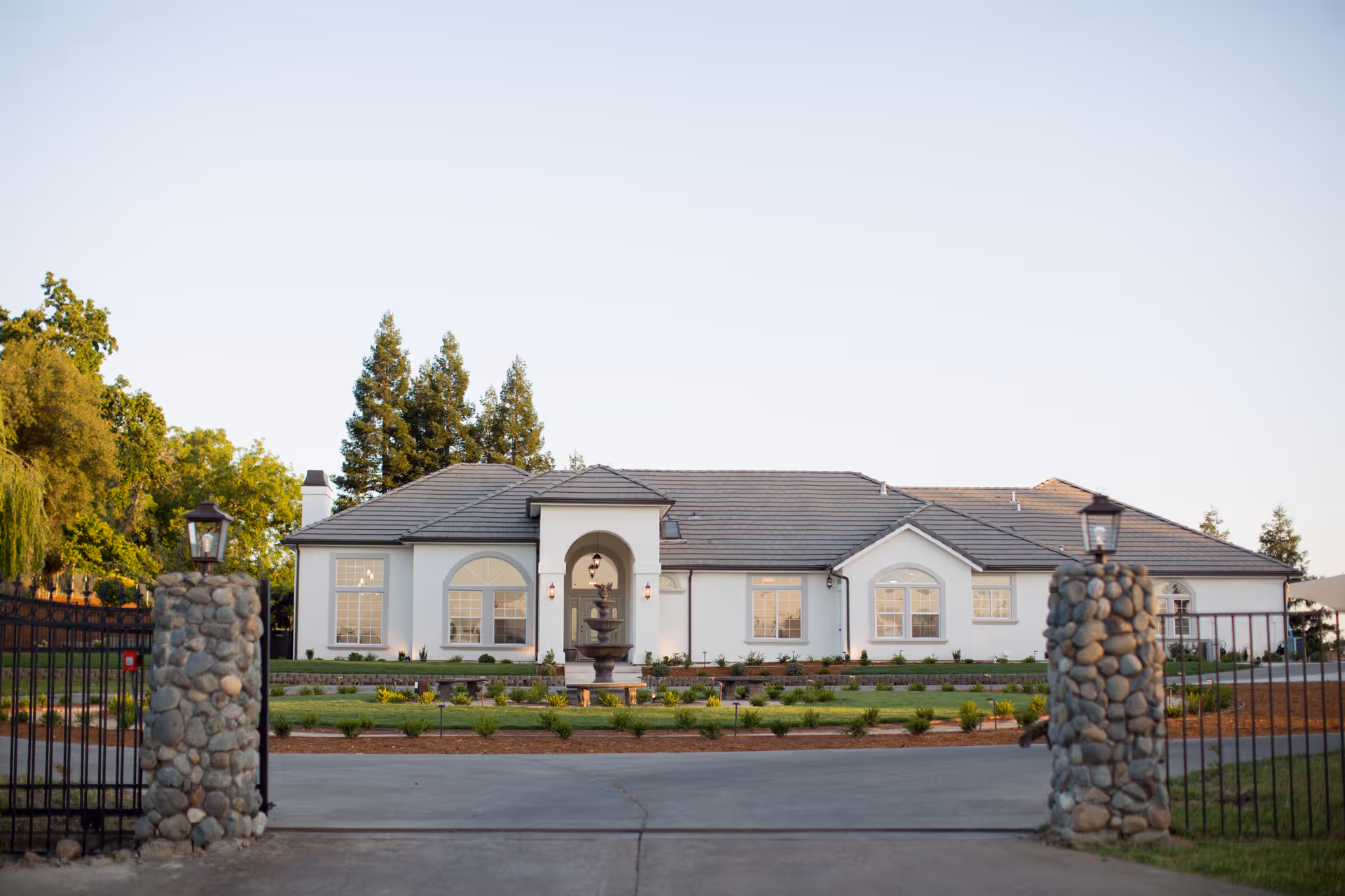 A single-story white senior living facility with a gated stone entrance and manicured lawn.