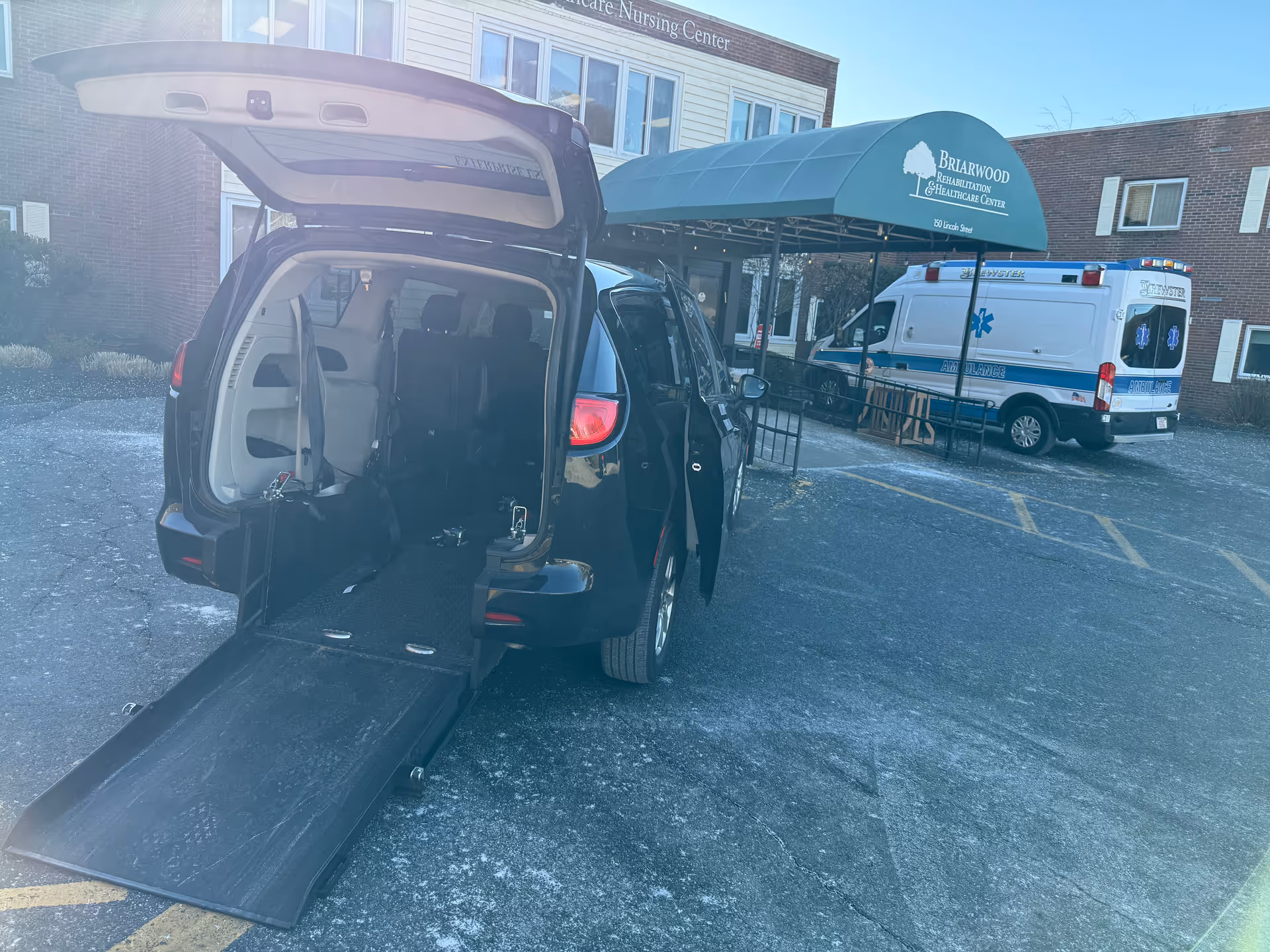 Back of a wheelchair-accessible van with ramp parked outside a healthcare facility entrance.