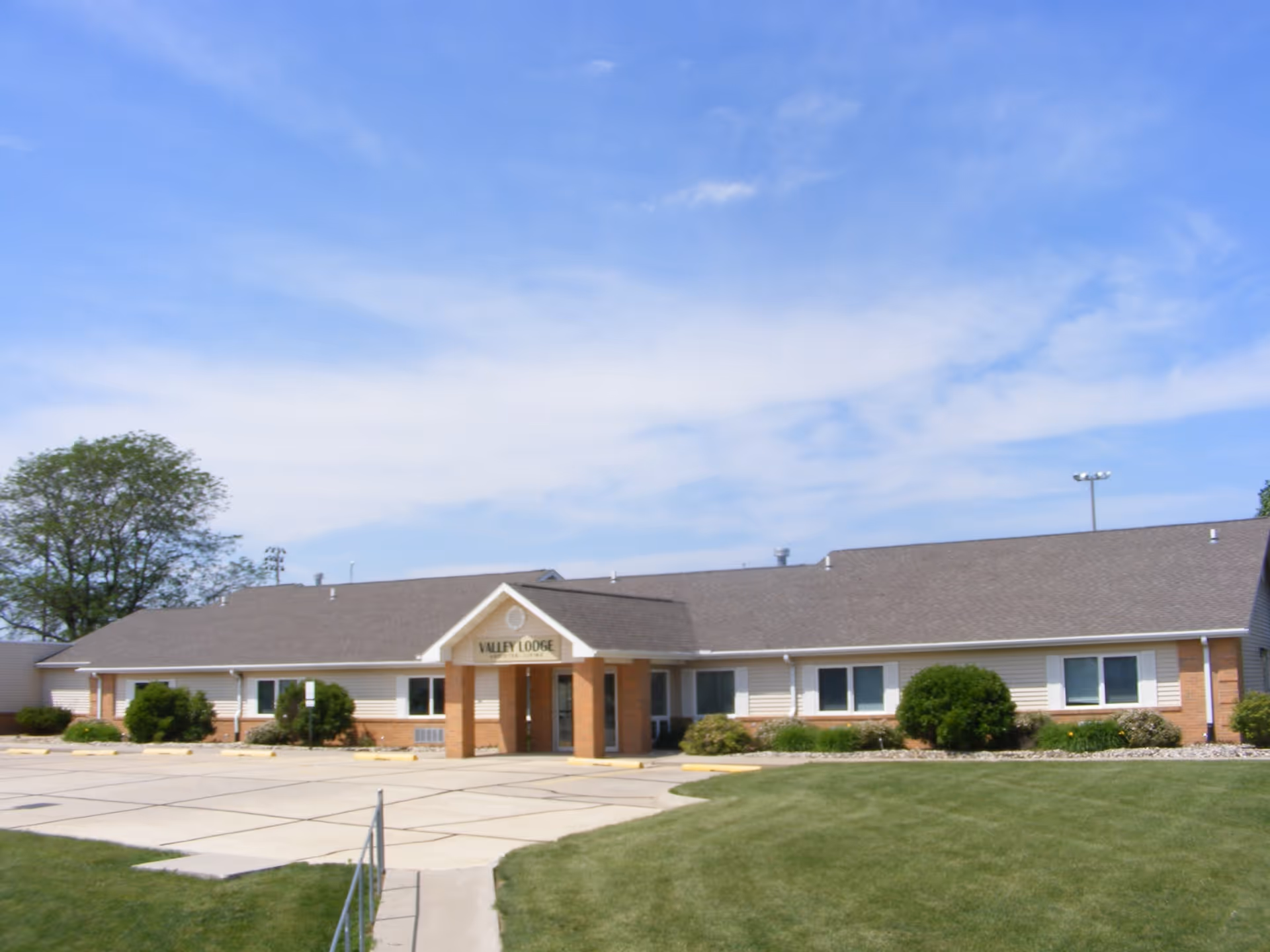 Exterior view of a single-story senior care building with a covered entrance and manicured lawn.