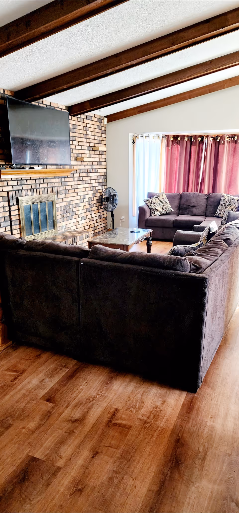 Cozy living room with a brick fireplace, dark sectional sofa, and mounted TV.