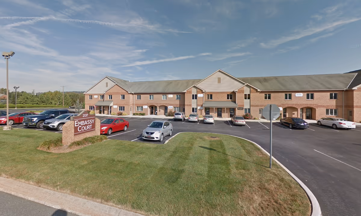 Exterior view of a brick senior living building with a parking lot and Embassy Court sign.