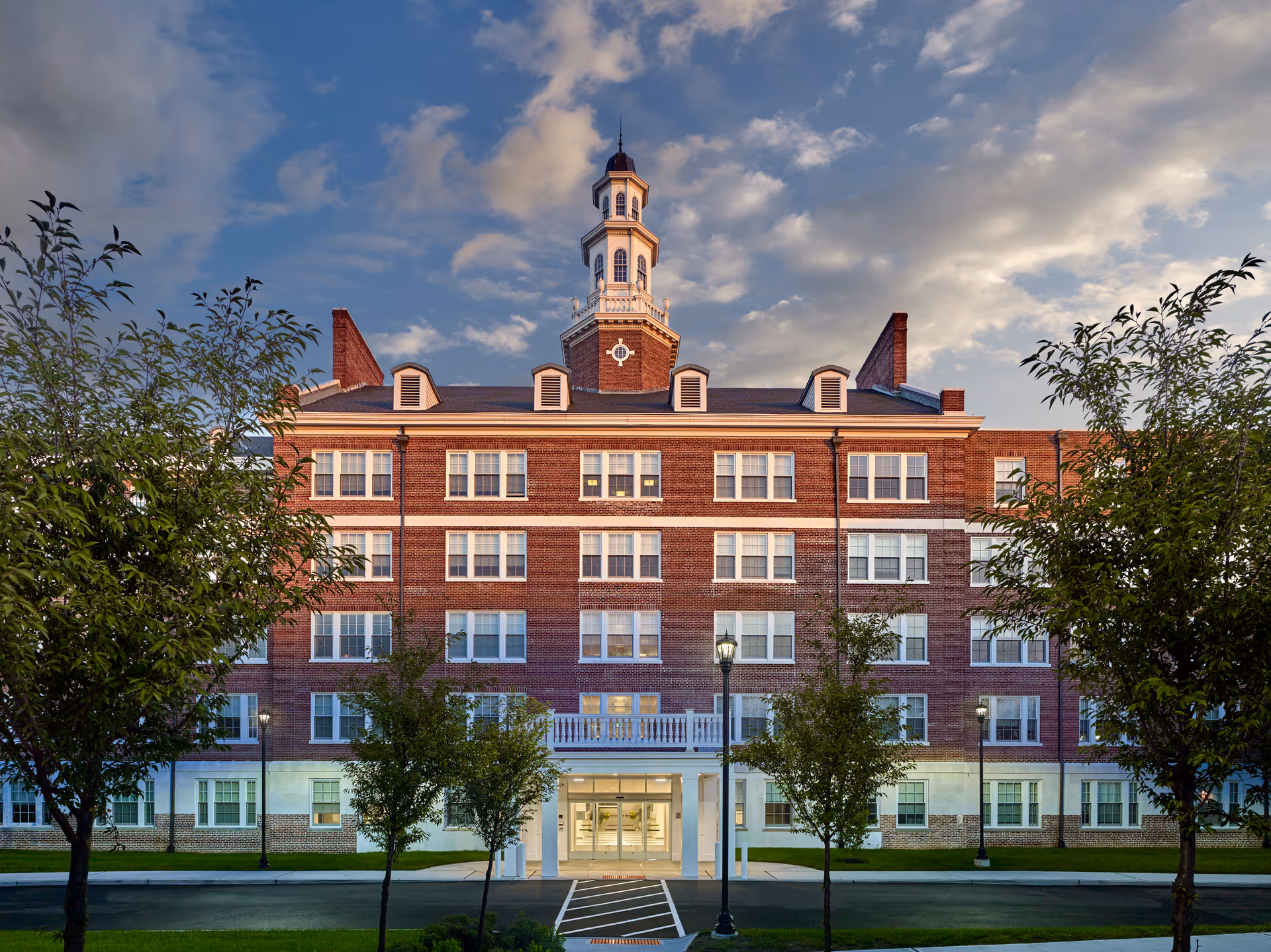 Brick senior living building with a central tower and welcoming entrance framed by trees.