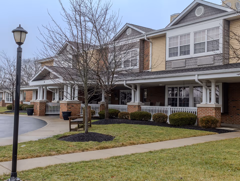 Two-story senior living facility with a covered porch, columns, and manicured landscaping.