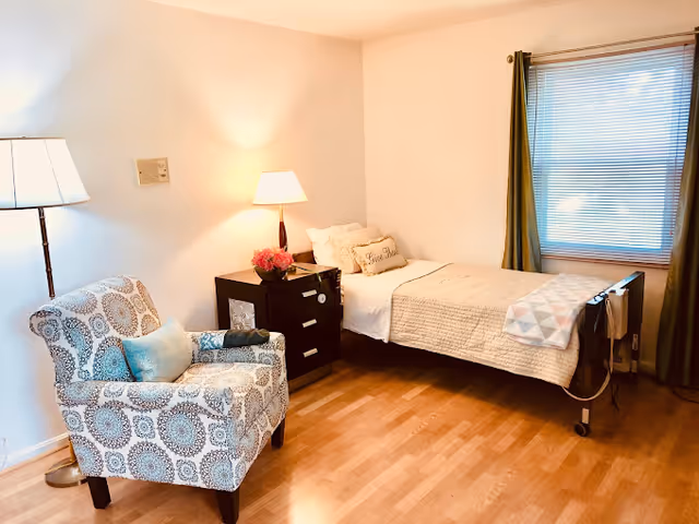 A neat bedroom in Allset Home-Health with a bed, chair, and lamps.