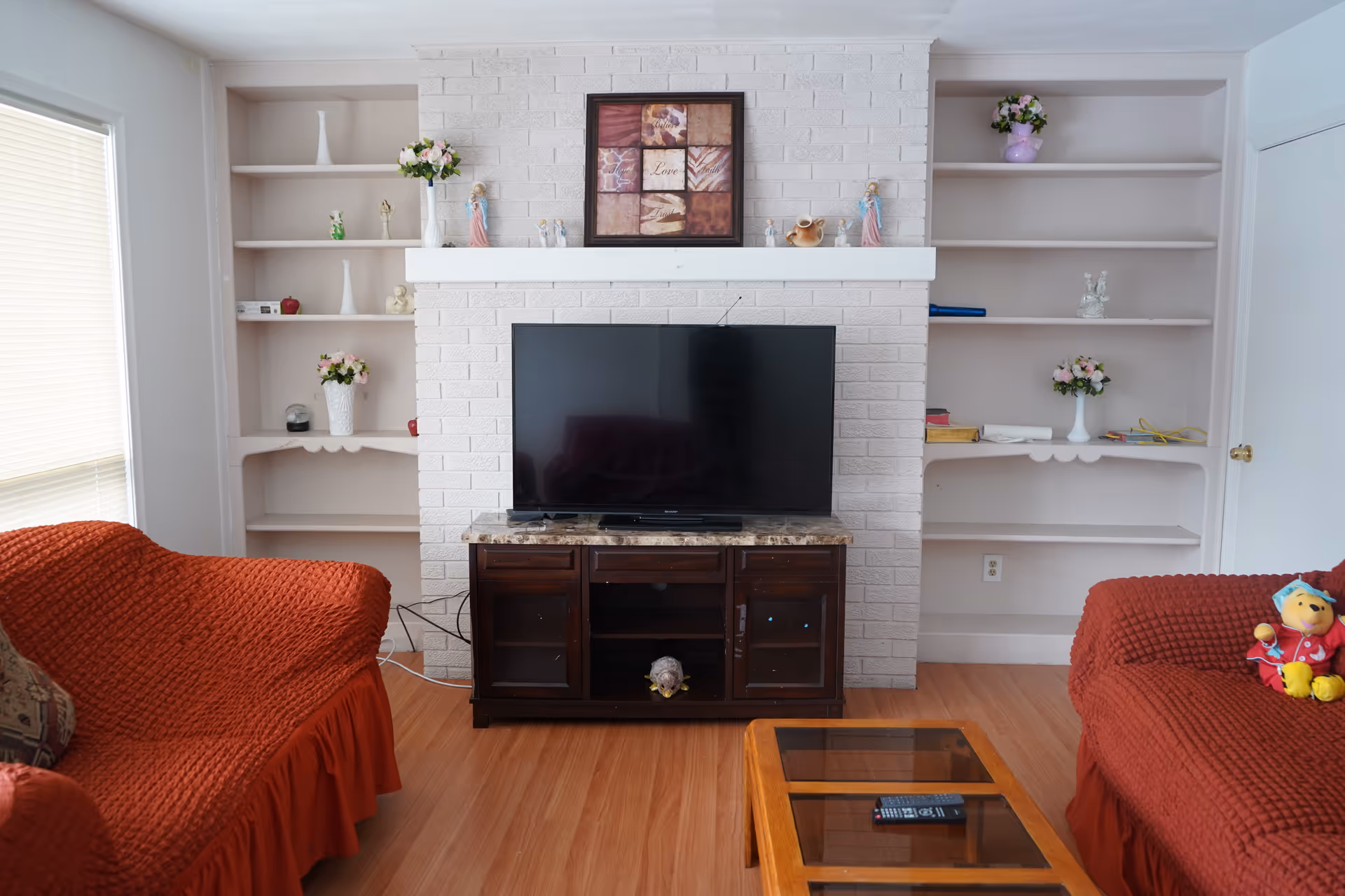 Divine Manor living room with a TV on a brick fireplace and built-in shelves.