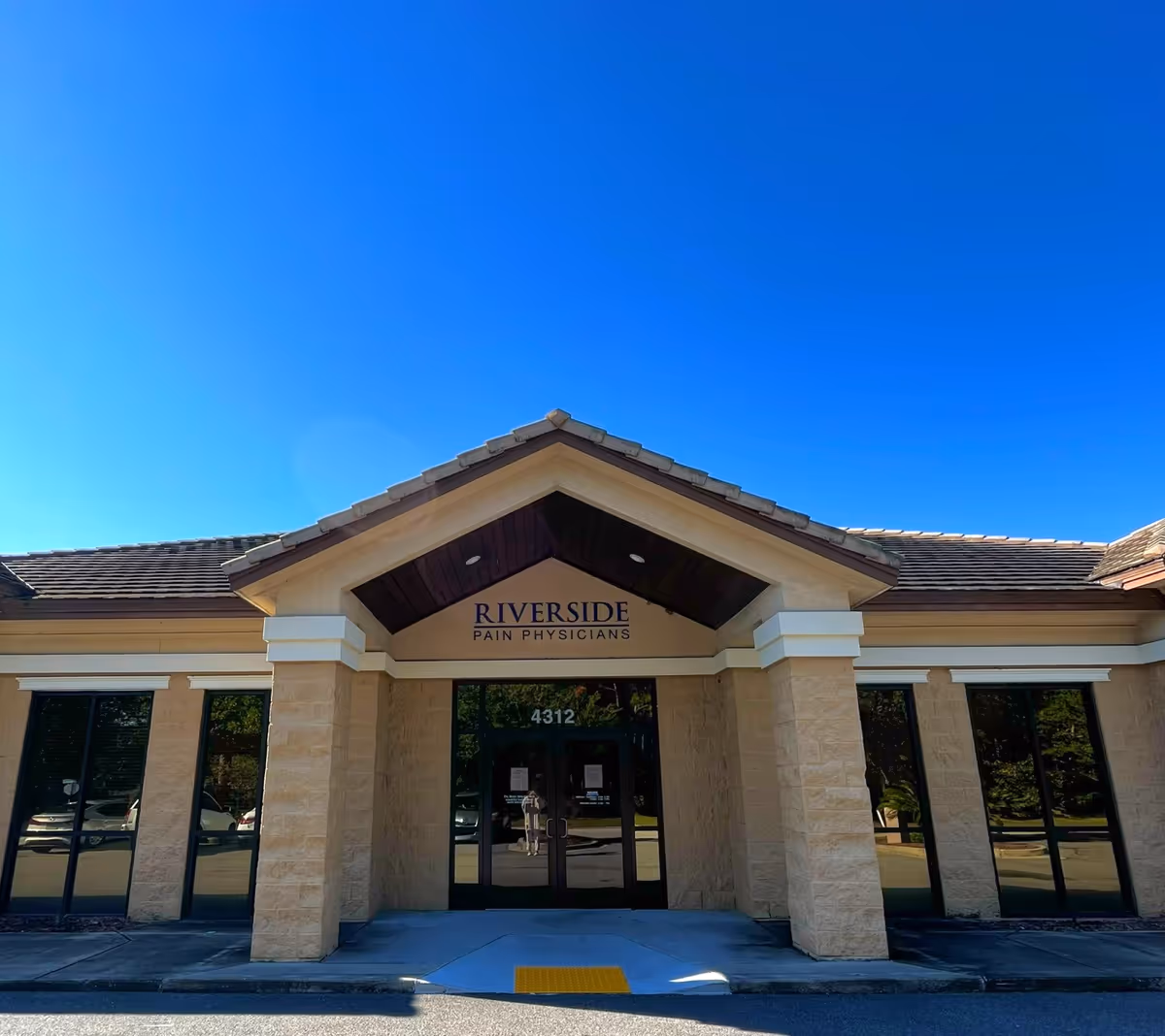 Front view of Riverside Pain Physicians building with entrance and sign under blue sky.