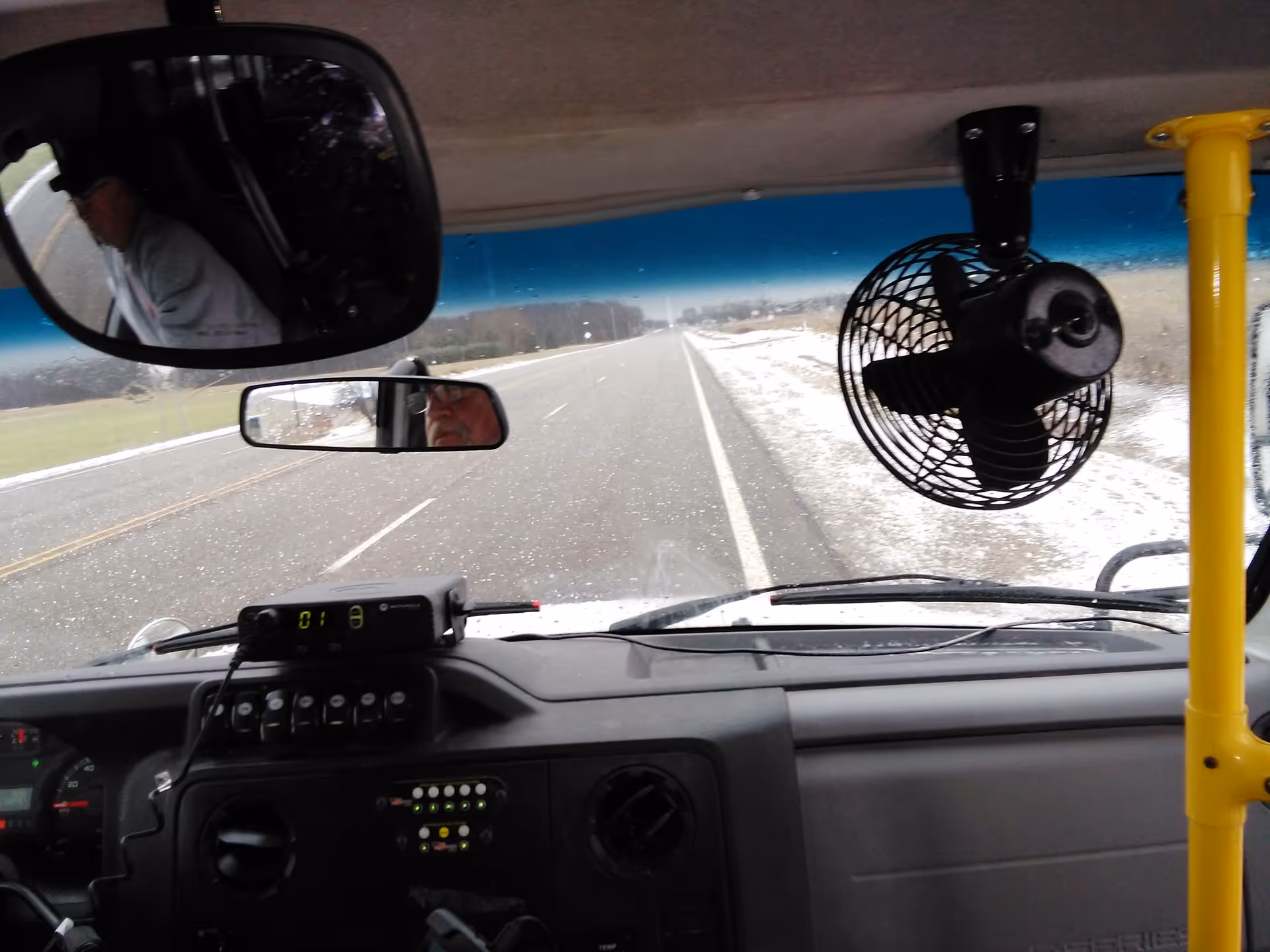Bus interior showing dashboard, rearview mirrors, and snowy road ahead.