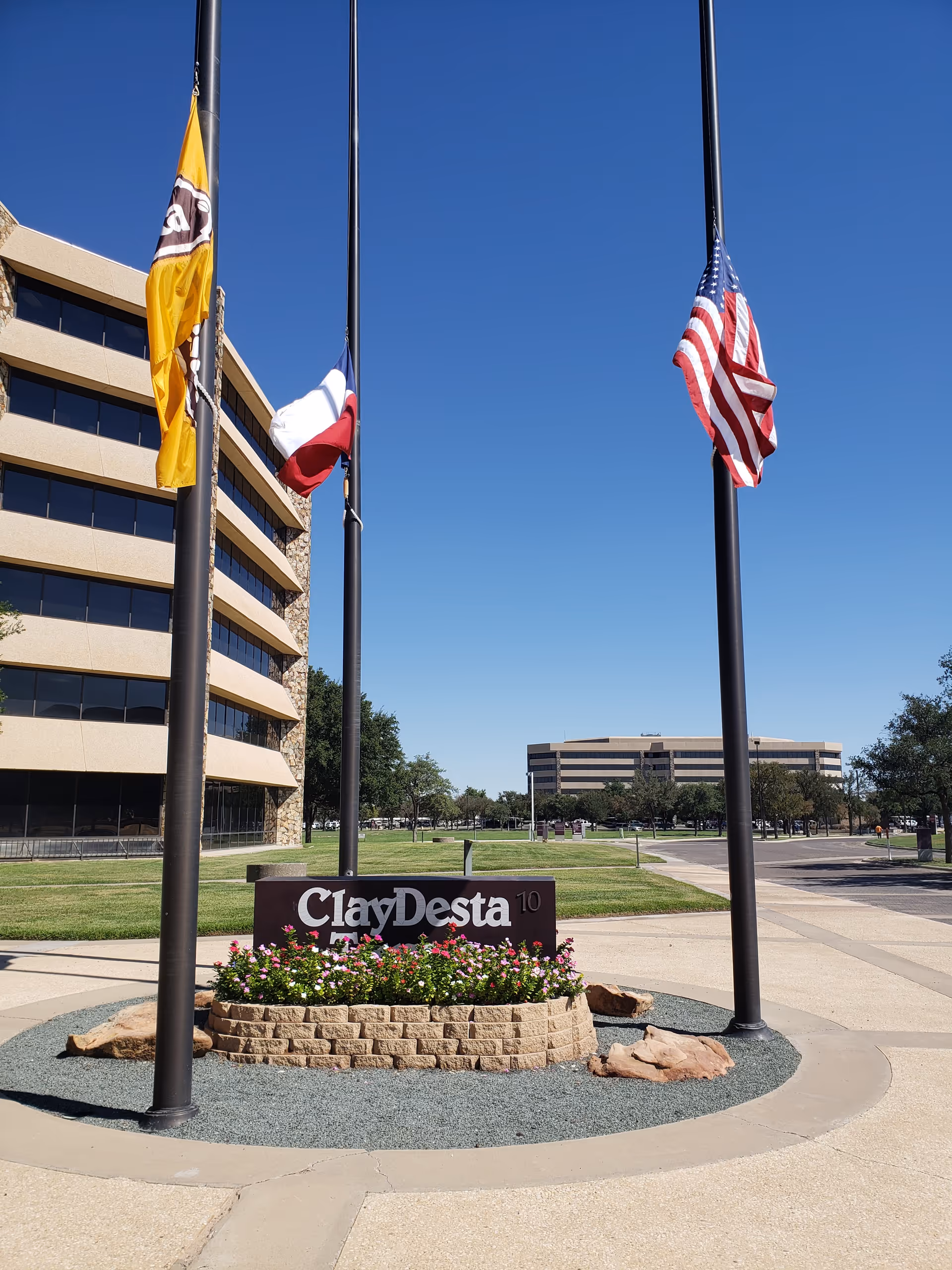 Exterior view of a corporate building with flagpoles, landscaping, and a circular flower bed.