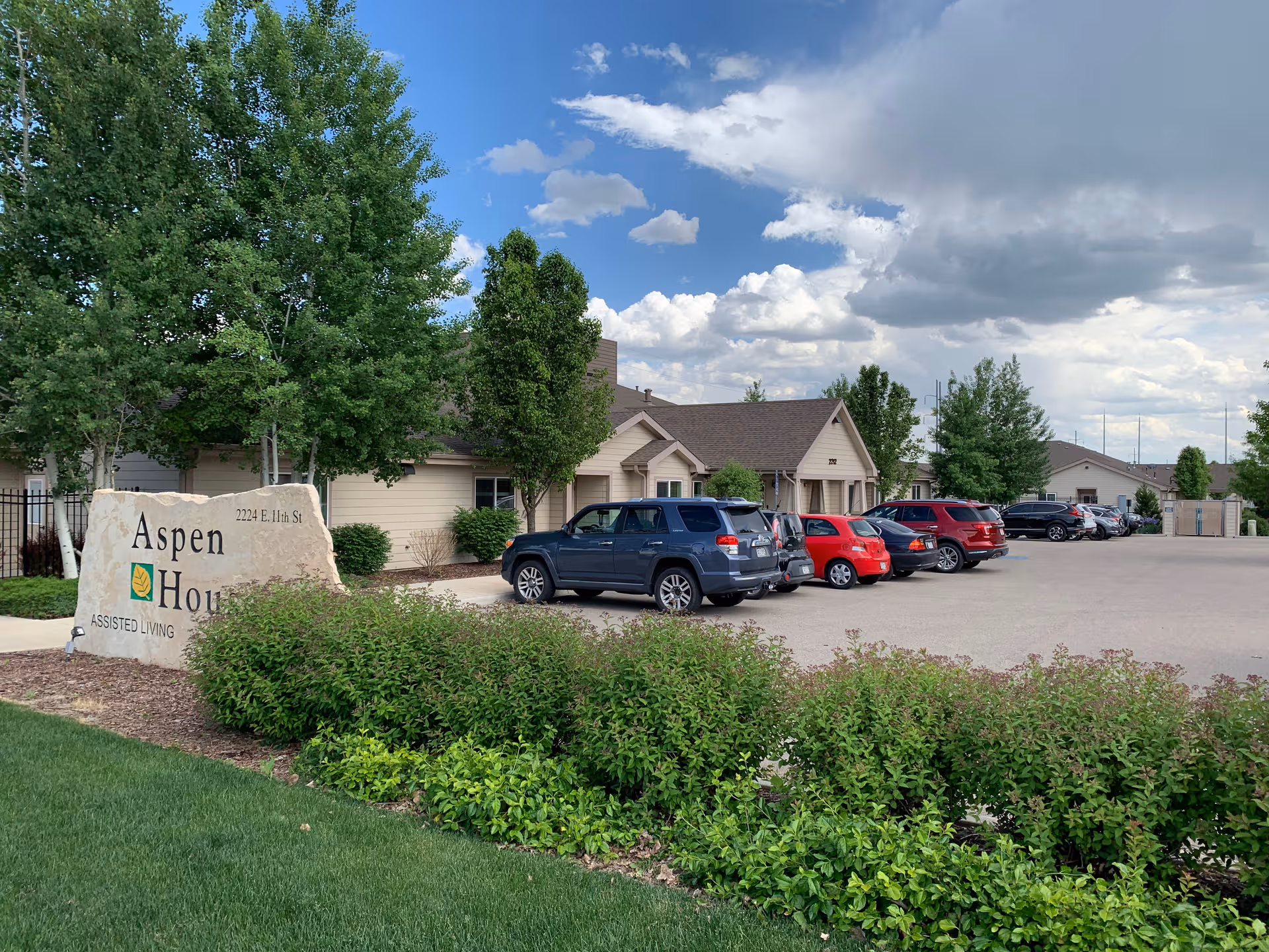 Exterior view of Aspen House assisted living with sign, trees, and parked cars.