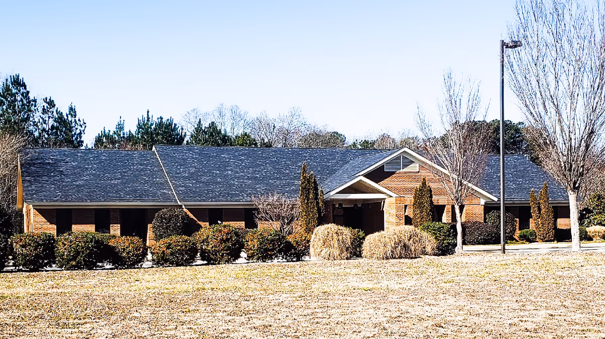 Single-story brick senior care facility front with trimmed shrubs and a lamppost.