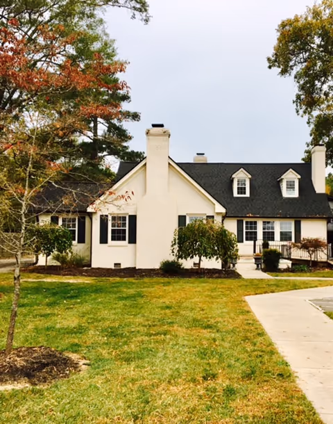 Front exterior of a white, residential-style senior living facility with a manicured lawn.