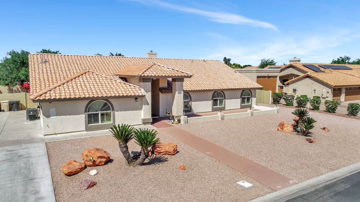 Single-story stucco house with a tiled roof, gravel front yard and desert landscaping viewed from the street.