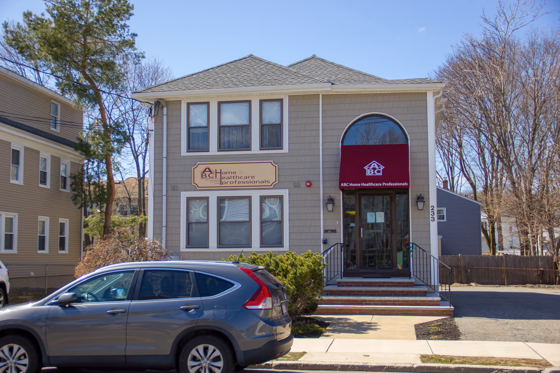Front of a two-story beige facility with ABC Home Healthcare Professionals sign and a car.