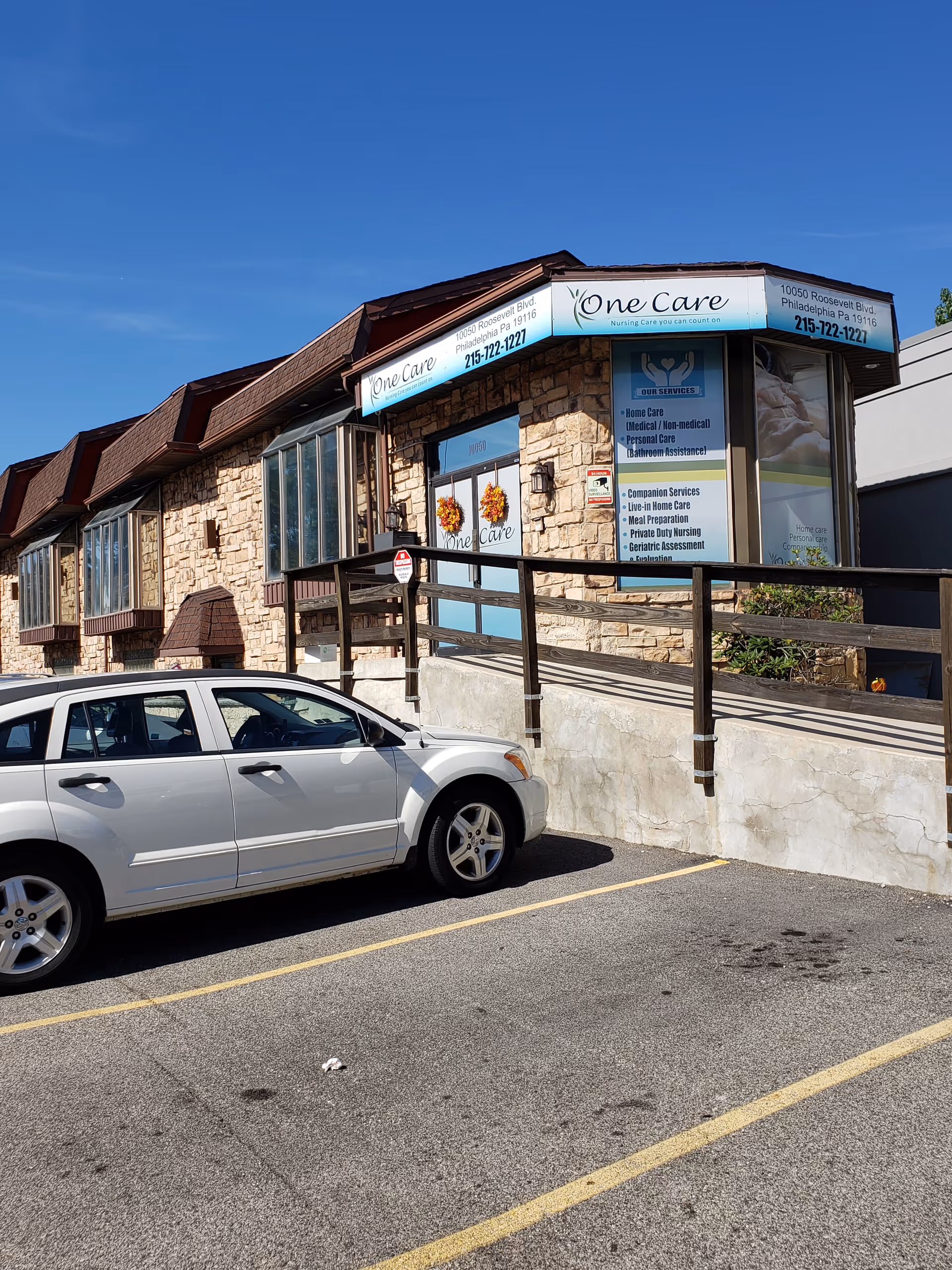 Stone exterior building with One Care sign and a parked white car in foreground