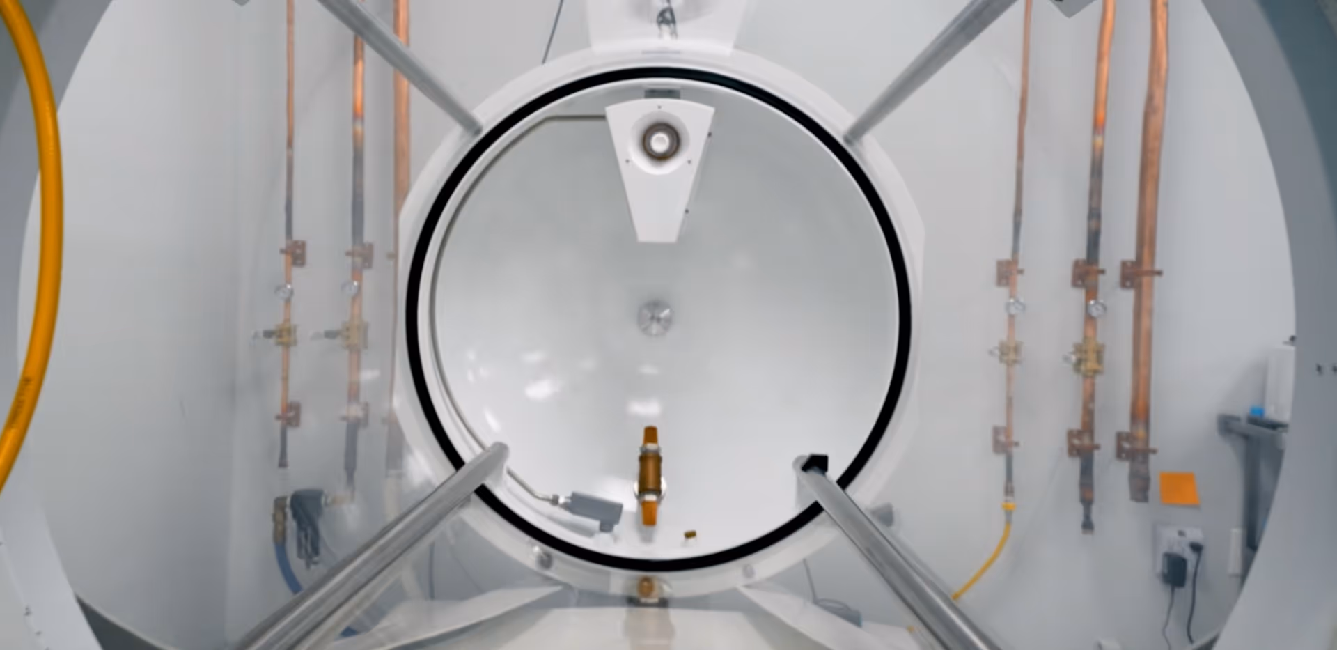 Hyperbaric chamber interior featuring a circular door and copper piping along both sides.