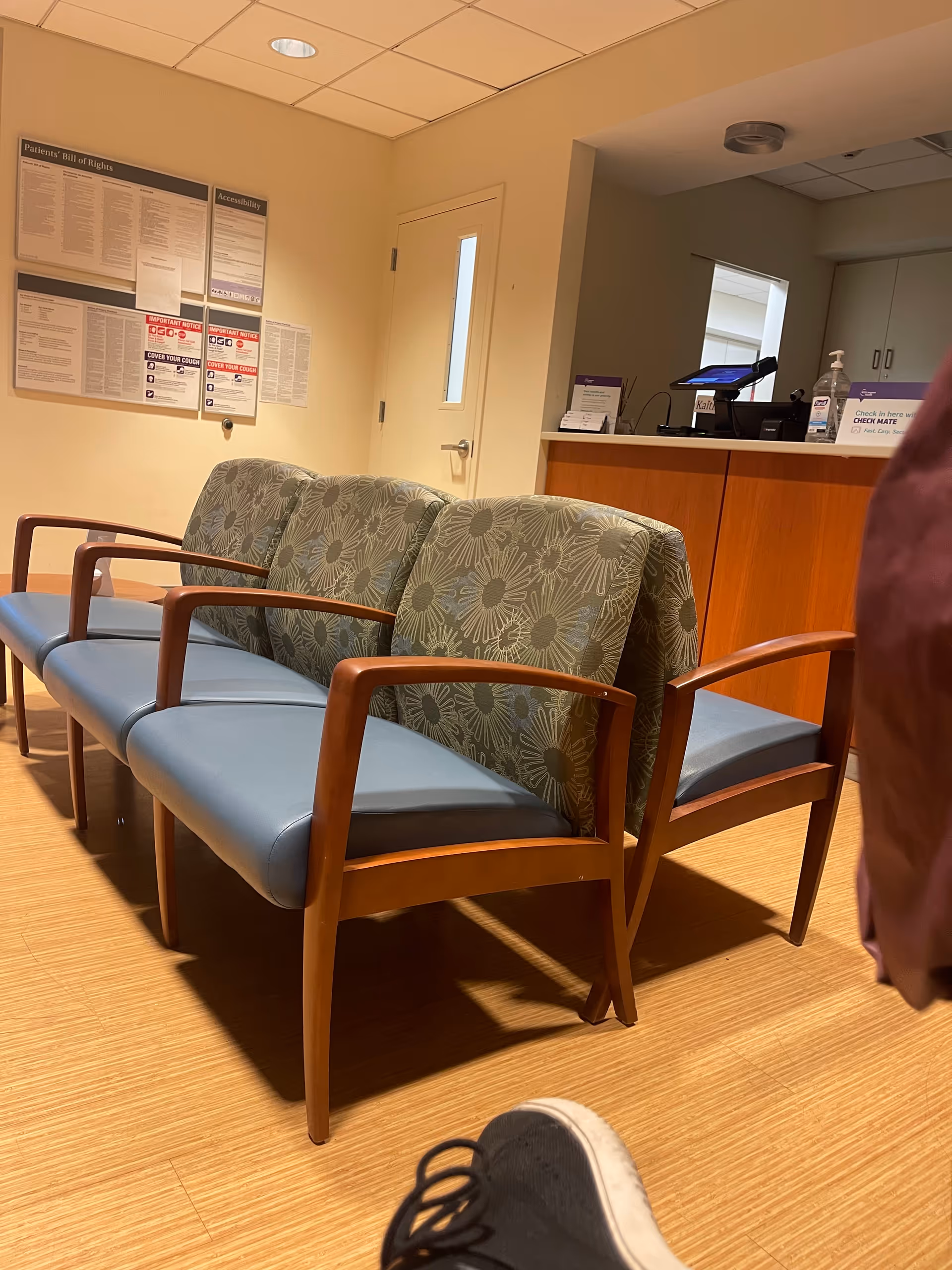 Interior waiting area with blue cushioned chairs and a wood-front reception desk.