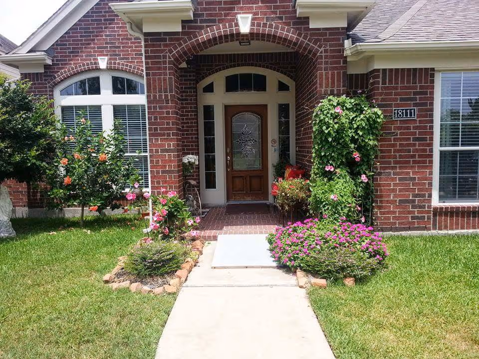 Brick building entrance with arched doorway, blooming flowers, and a manicured lawn.
