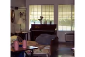 A cozy senior living room featuring a piano, sofa, chairs, and large windows.