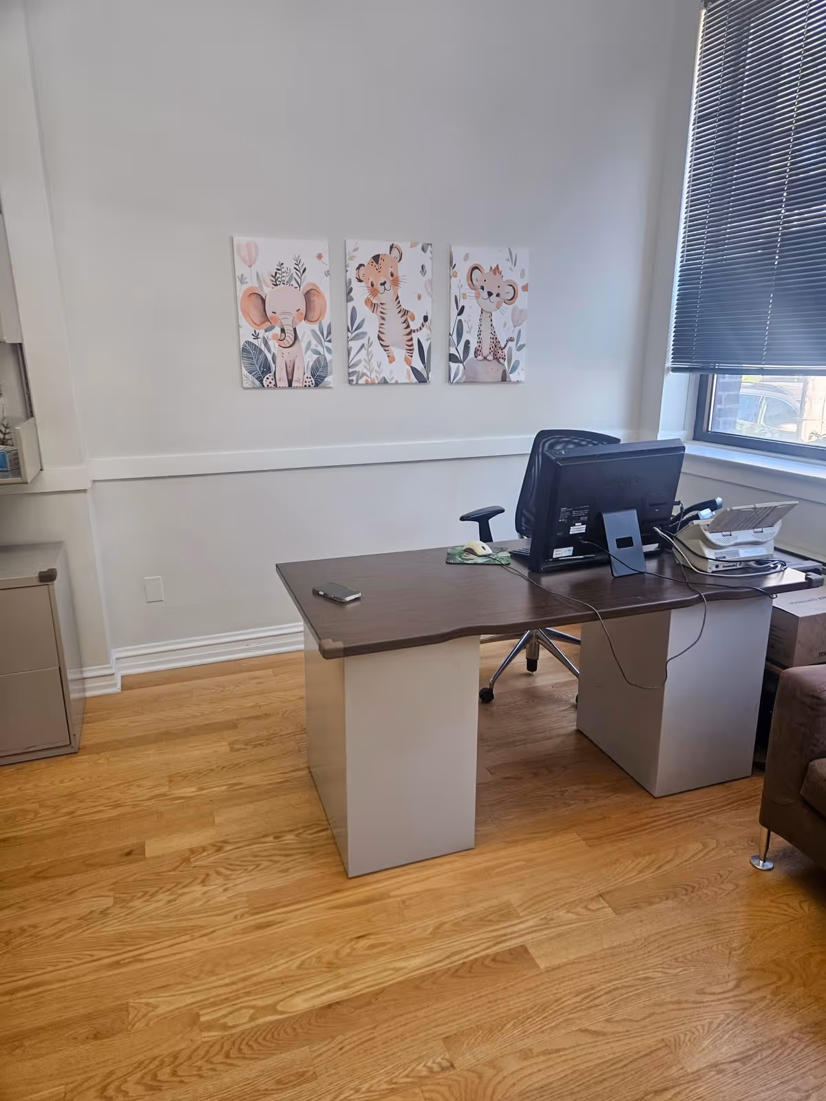 Office desk in a senior facility with computer, printer, and wall art by a window.