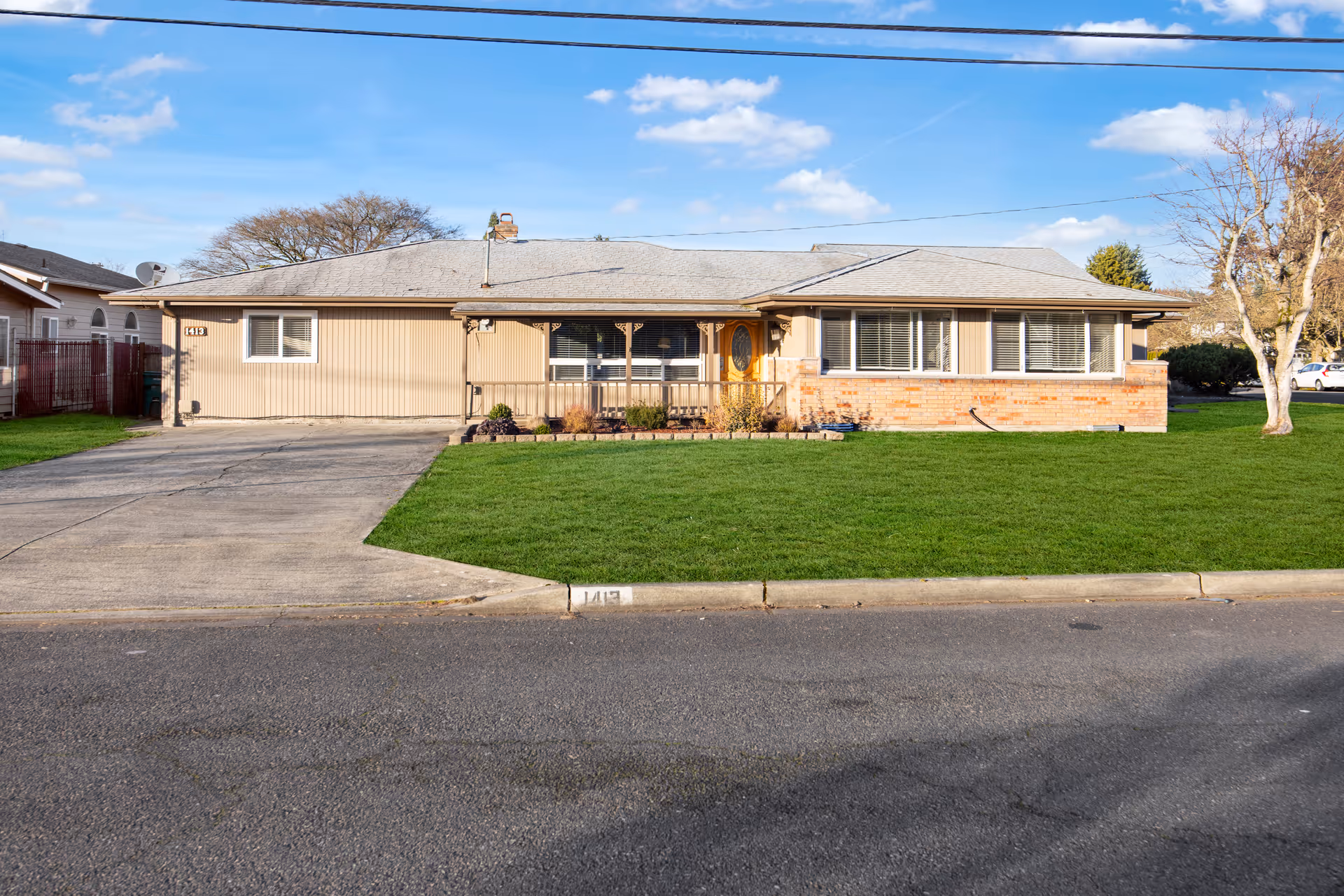 Exterior view of a single-story beige-siding building with a brick base and lawn.