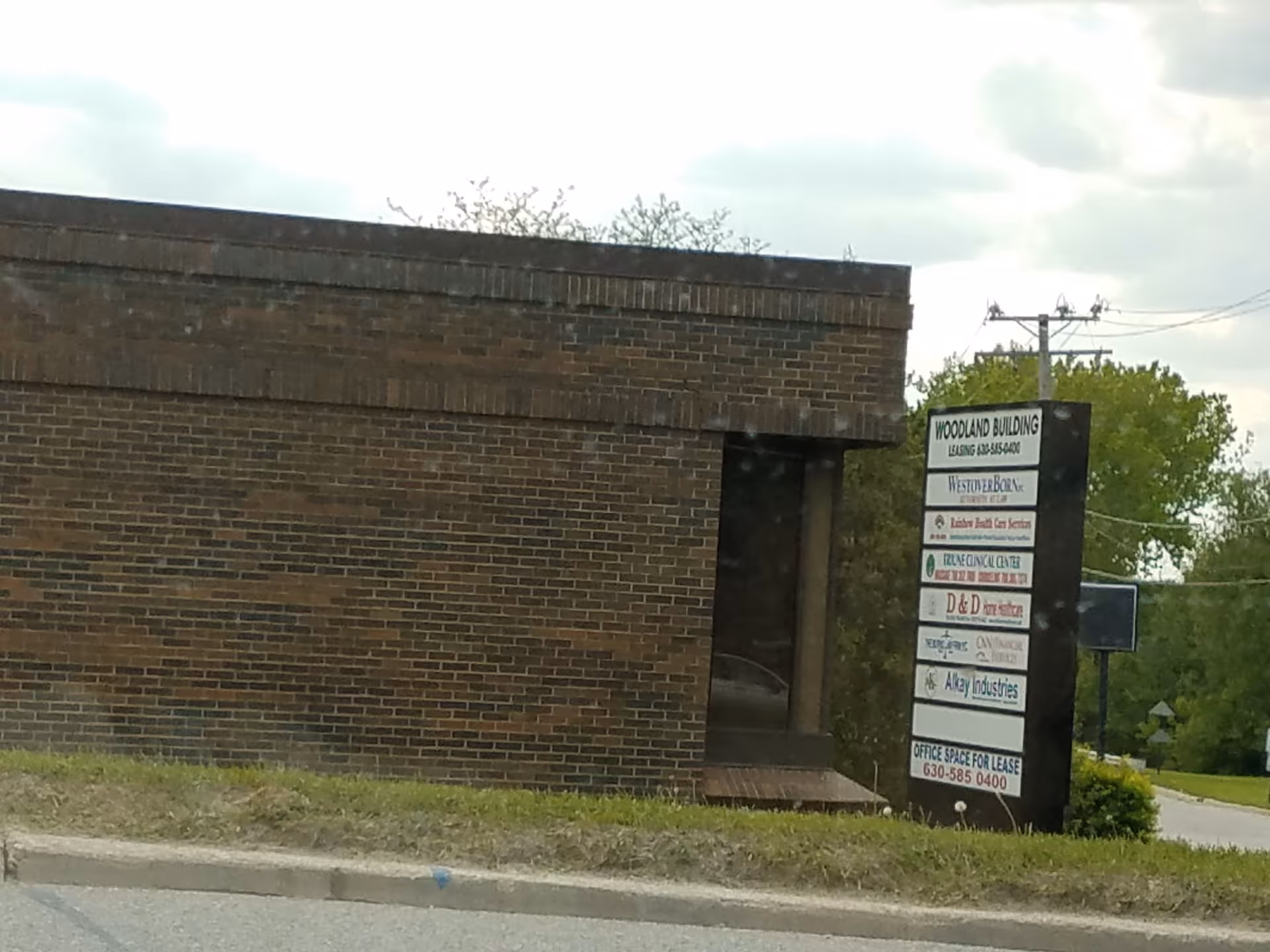Brick building exterior with a tall sign listing tenants beside a sidewalk.