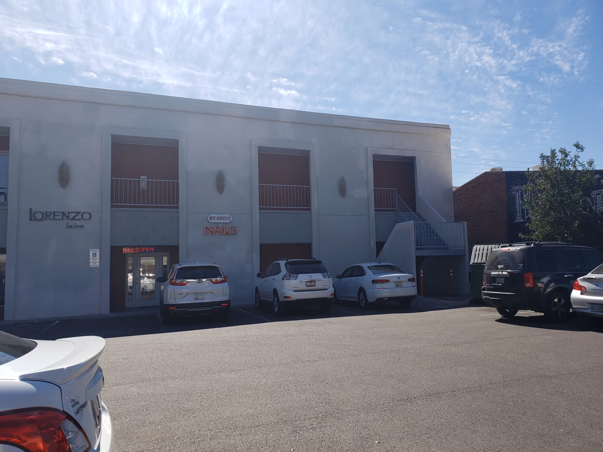 Gray two-story commercial building with storefronts and parked cars in front.