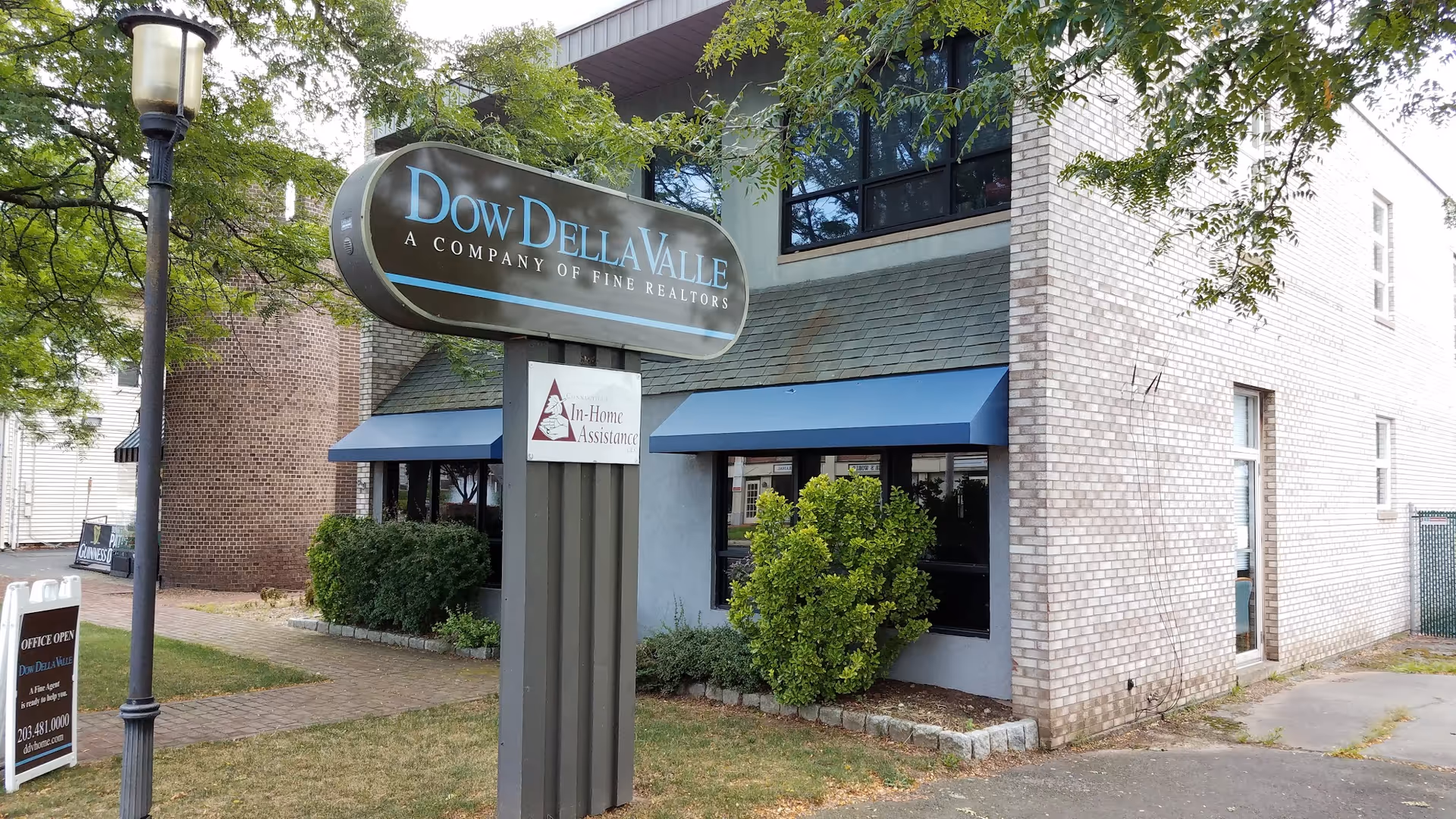 Exterior brick building with blue awnings and an In-Home Assistance sign in front.