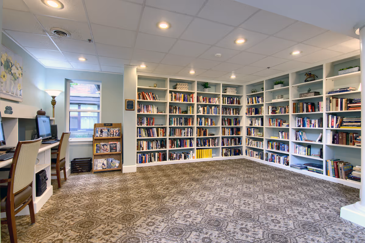 Carpeted common room with built-in bookshelves filled with books, computer workstations and a magazine rack.