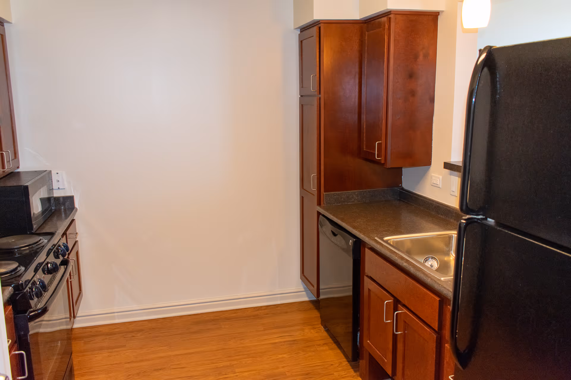 Compact kitchen with dark countertops, wooden cabinets, sink, dishwasher, stove, and refrigerator.