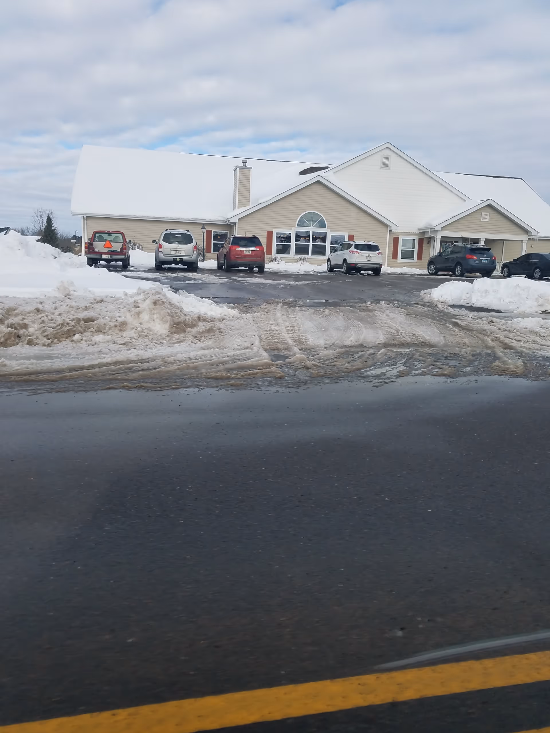 Snow-covered senior living facility building with a parking lot in front.