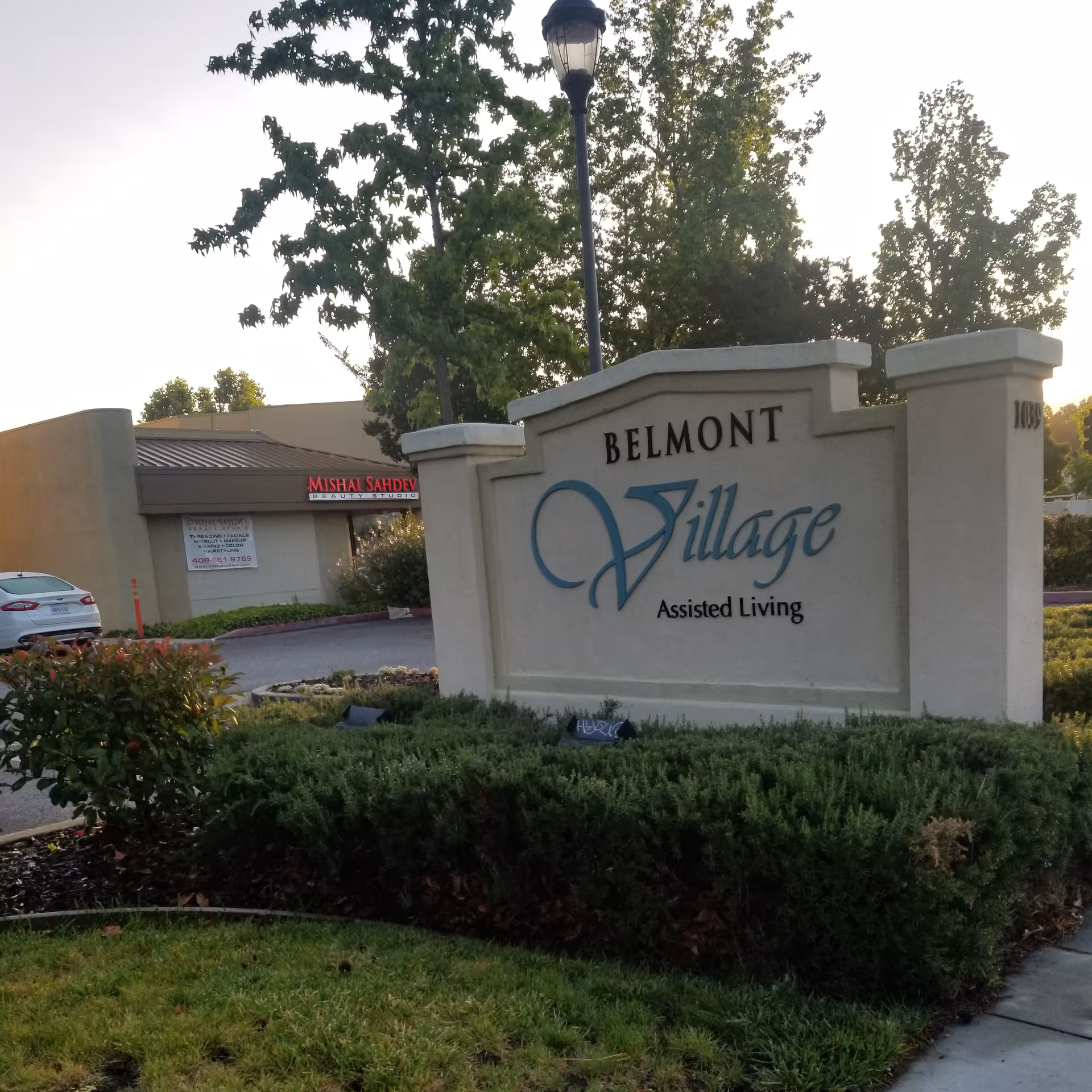 Entrance sign reads Belmont Village Assisted Living Sunnyvale with landscaping and trees.