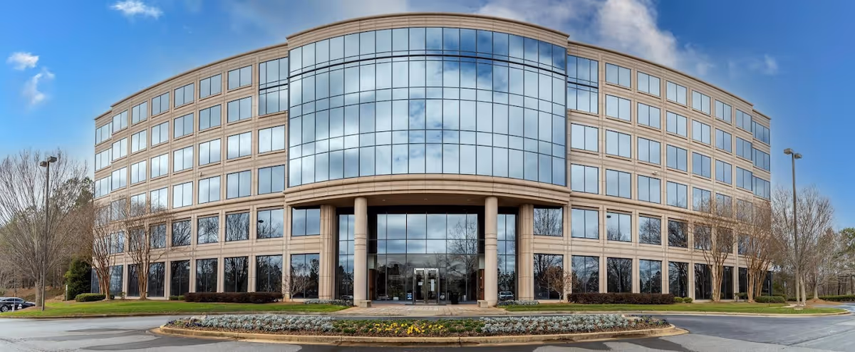 Modern glass-front building with curved entrance, tall pillars, and landscaped front circle.