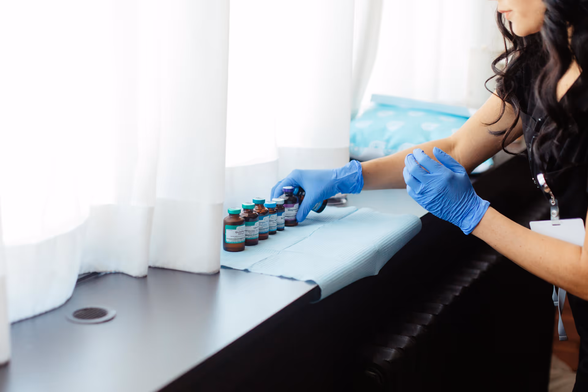 Gloved caregiver arranges small medical vials on a windowsill inside a senior living facility