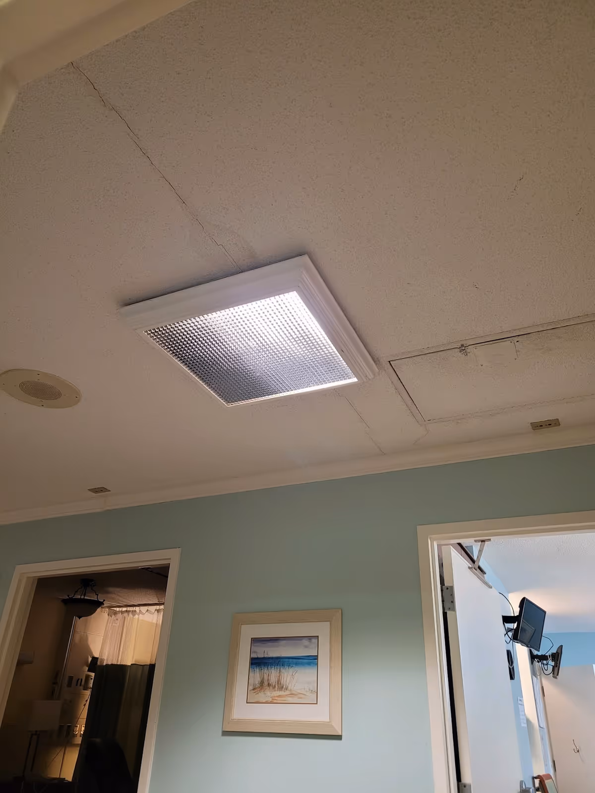 Interior hallway ceiling with fluorescent lights, blue wall, beach-themed art, open doorways.