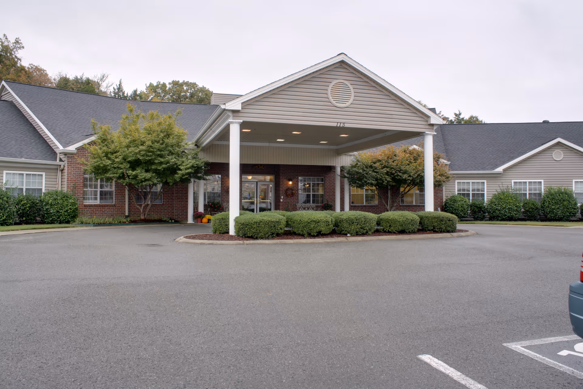 Exterior of Lincoln Manor senior living facility with a porte-cochère, shrubs, and a parking lot.
