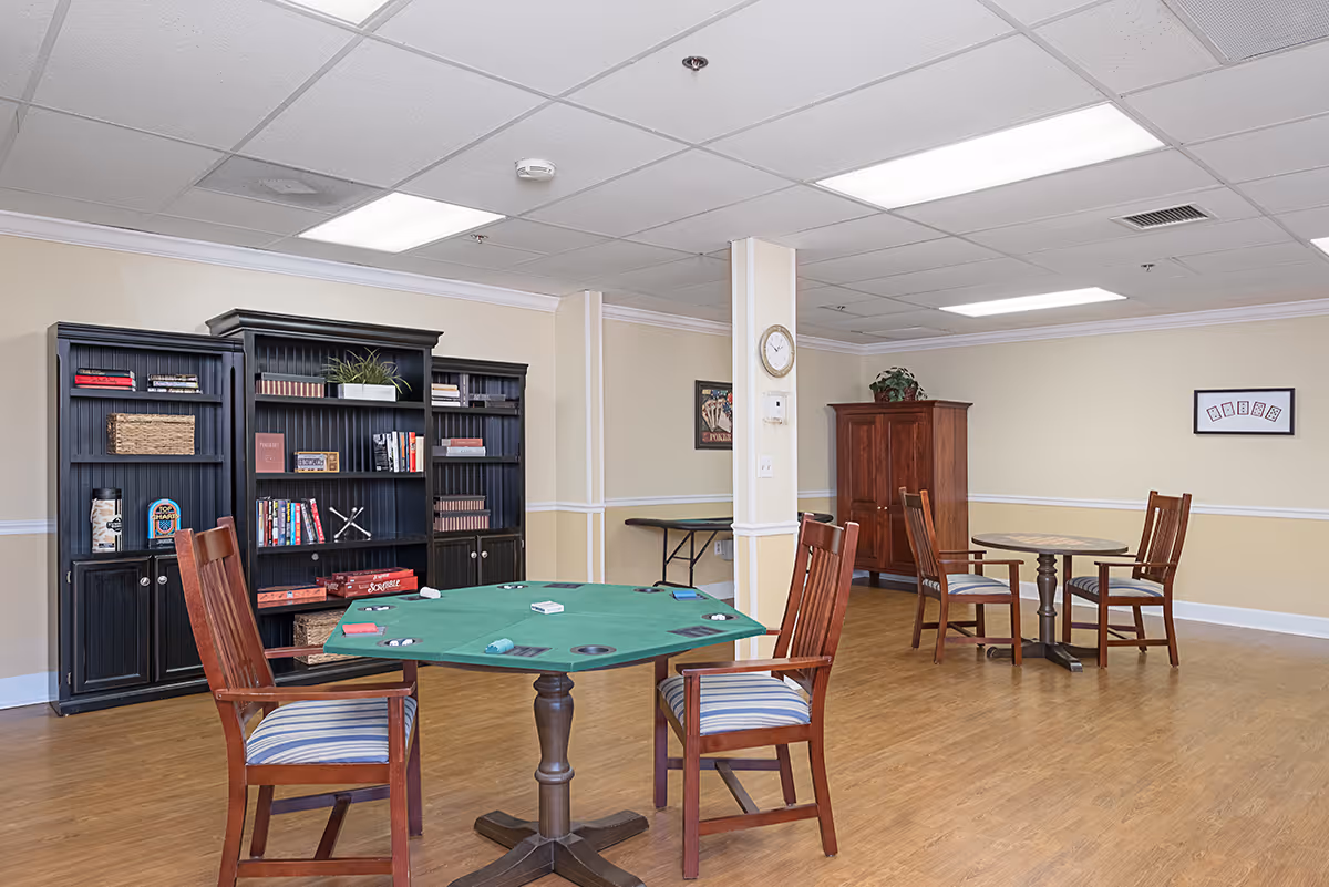 Interior activity room with a green poker table, chairs, bookshelves, and a round table.