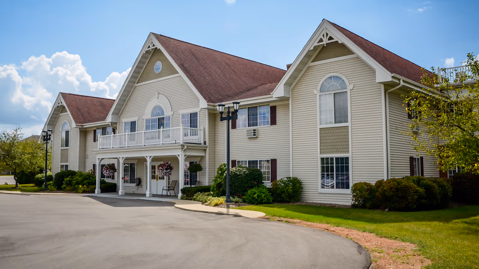 A beige senior living facility with arched windows, balconies, and a covered entrance.