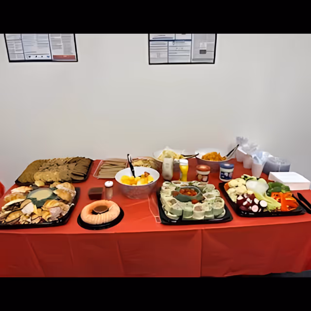 A long buffet table with assorted foods on a red cloth against a white wall.