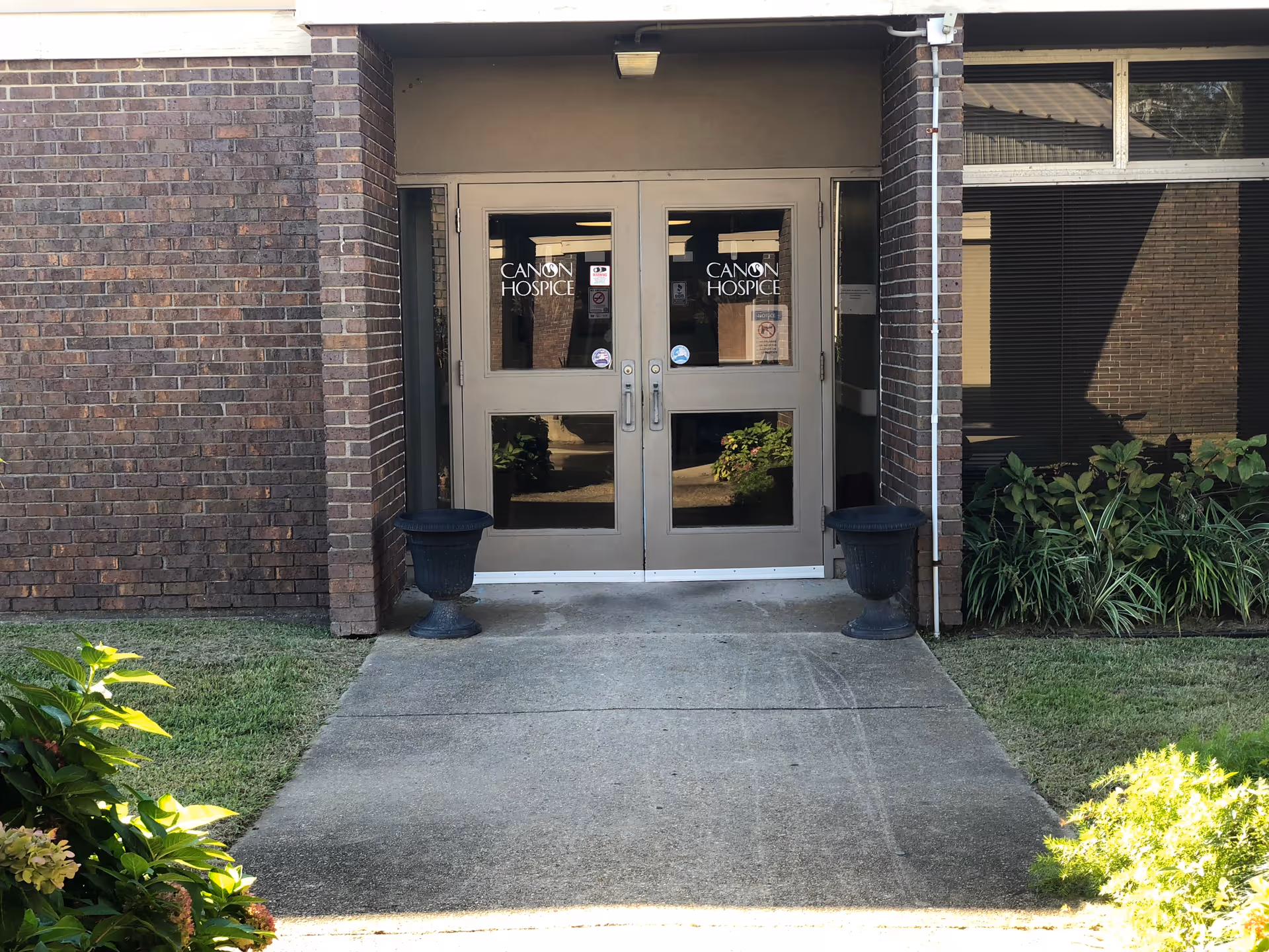 Brick building entrance with double doors labeled Canon Hospice, flanked by planters.